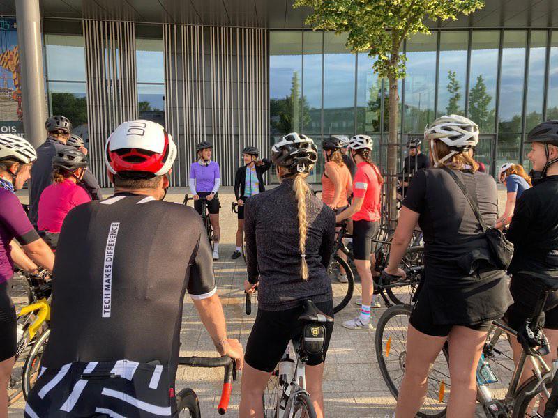 Viele Radfahrer stehen vor einem Museum in Sportkleidung.