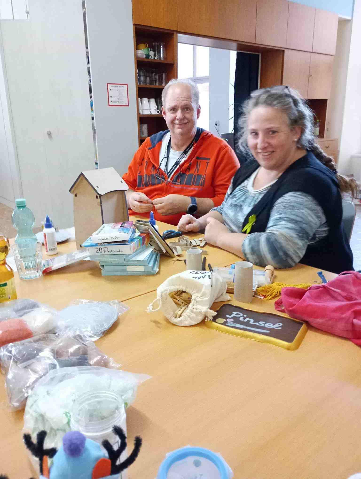 Ein Mann und eine Frau sitzen am Basteltisch beieinander.