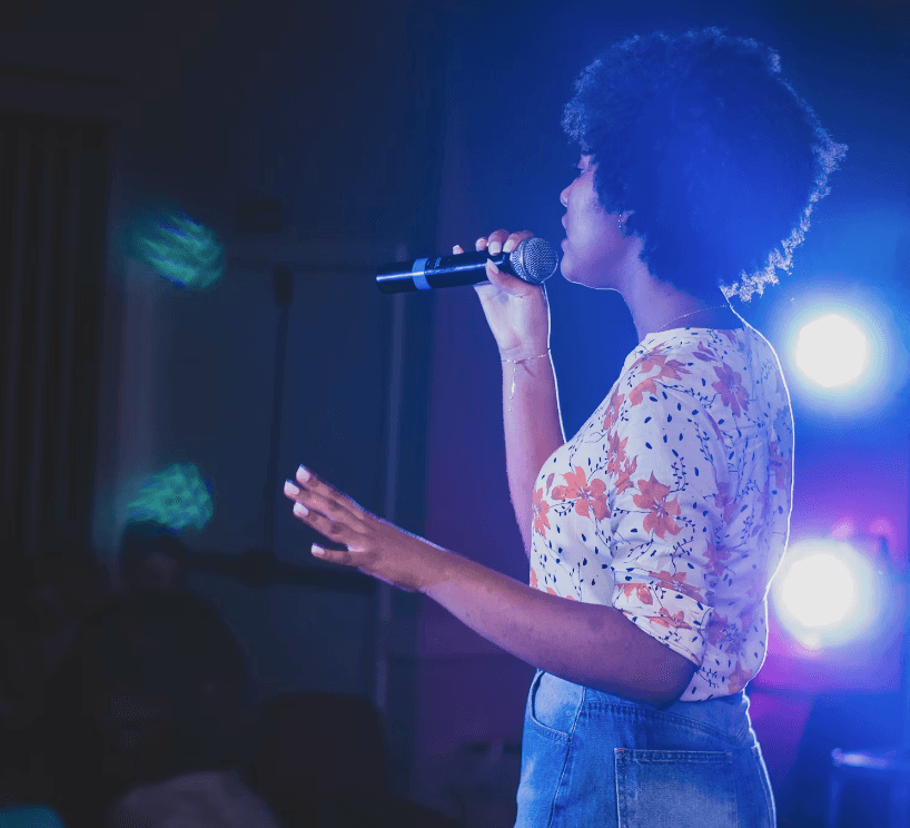 Eine junge Frau mit Afro, die vor Publikum singt, stellvertretend für das Karaoke im MGH