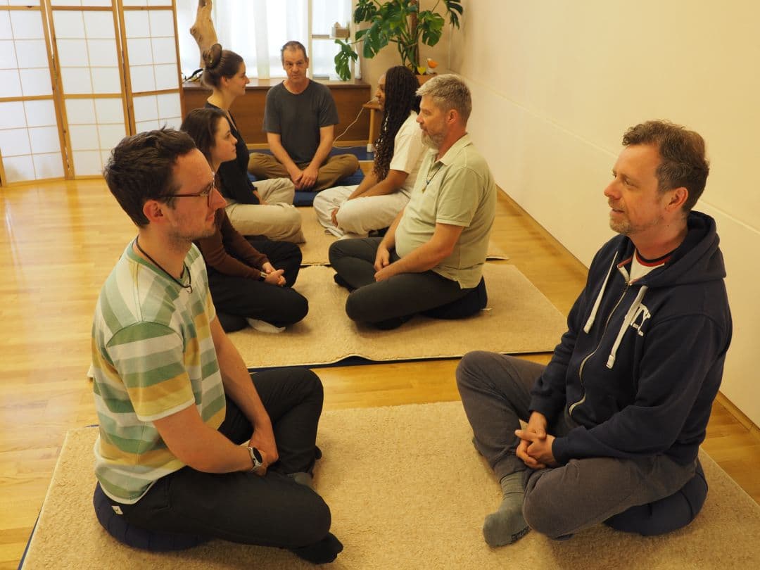 Mehrere Personen, die im Dyaden-Format gegenüber sitzen, um miteinander zu sprechen. Am Anfang der Sitzgruppen sitzt der Feldenkreis-Lehrer Franz-Joseph Schumeckers.